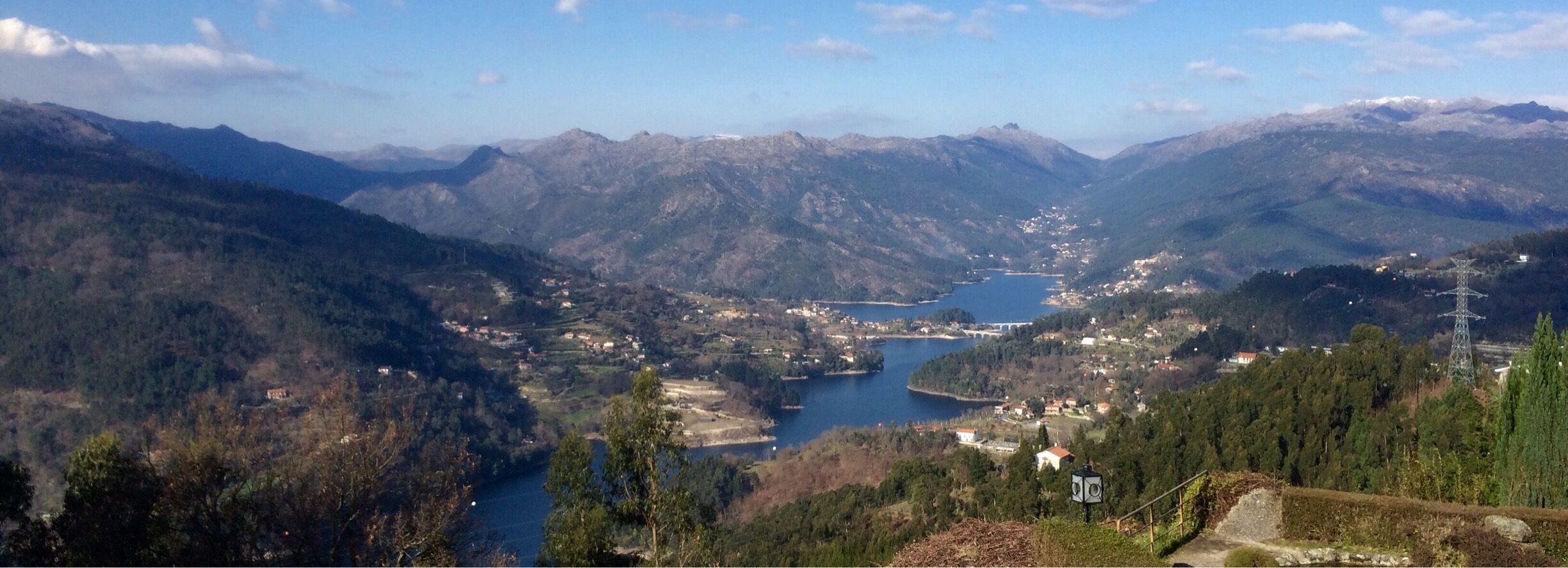 A mountainous landscape with a lake, scattered houses, and a power line tower.
