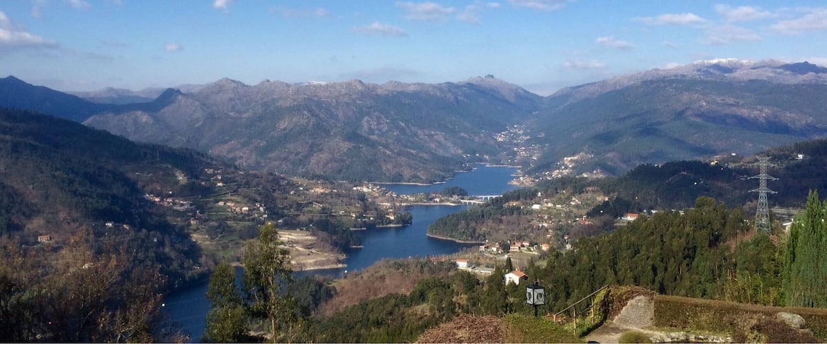 A mountainous landscape with a lake, scattered houses, and a power line tower.