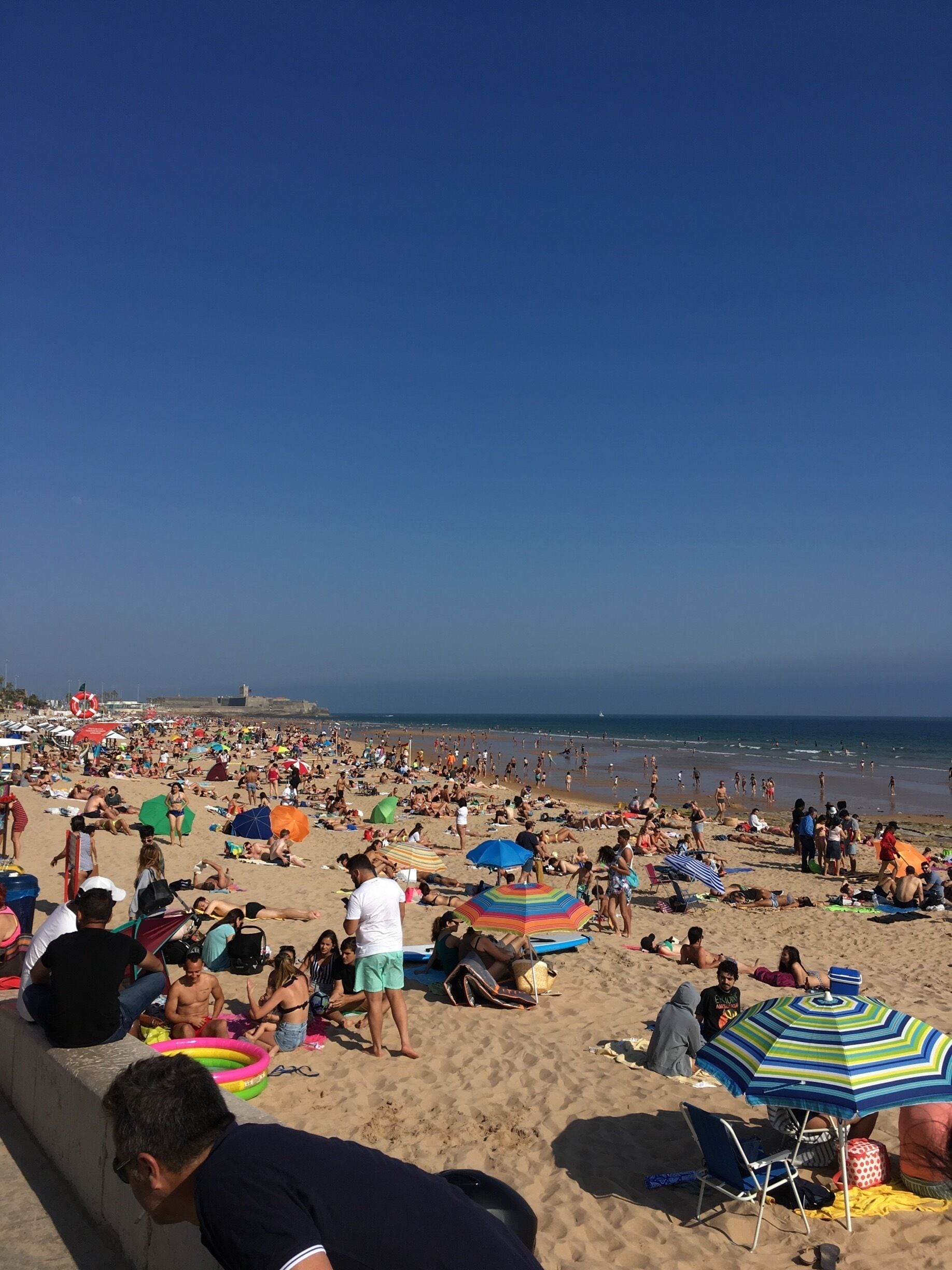 A crowded beach with people sunbathing and swimming.