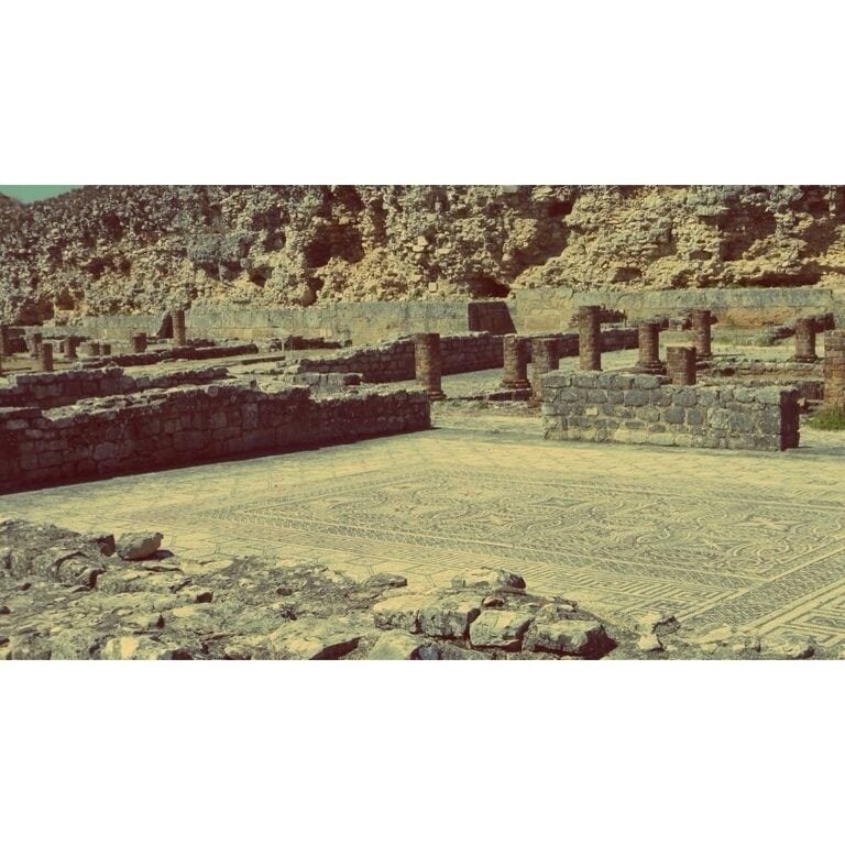 Ruinas antiguas con columnas de piedra y un suelo con diseño.