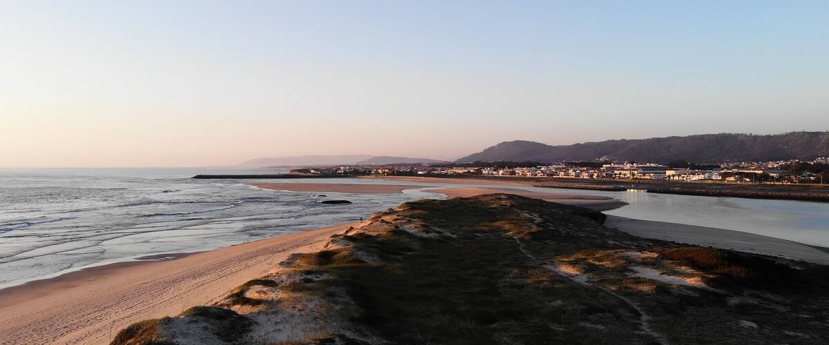 A coastal landscape with a sandy beach, calm sea, and a distant town.