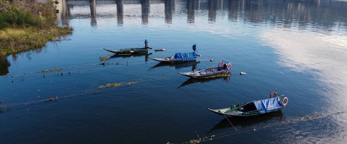 A calm river with several boats anchored near a bridge.