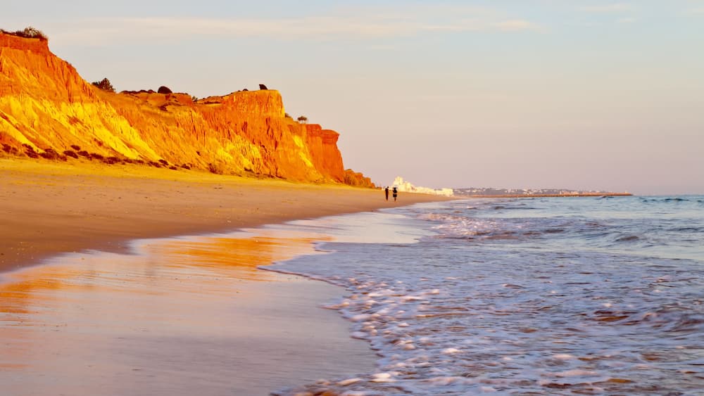 Beautiful Praia da Falesia near the city of Vilamoura with a shallow sandy beach fringed with unusual red rocks at sunset. Algarve, Portugal. Natural background. Summer holiday by the sea
