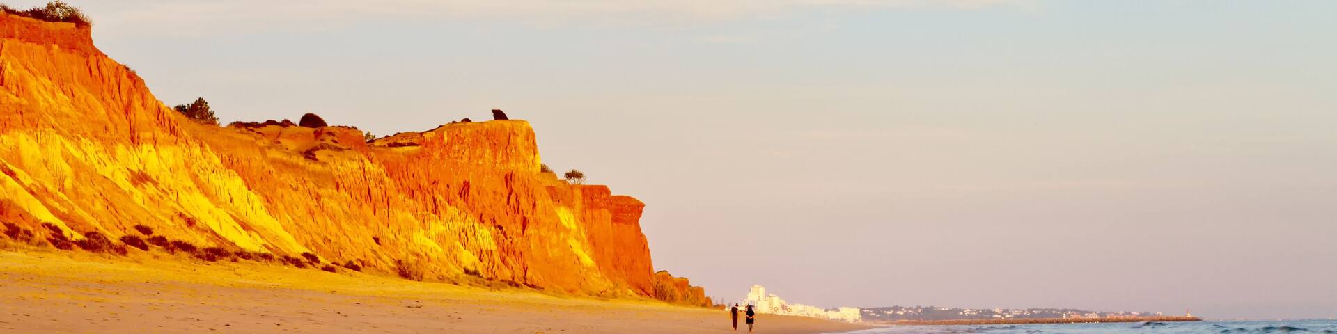 Beautiful Praia da Falesia near the city of Vilamoura with a shallow sandy beach fringed with unusual red rocks at sunset. Algarve, Portugal. Natural background. Summer holiday by the sea