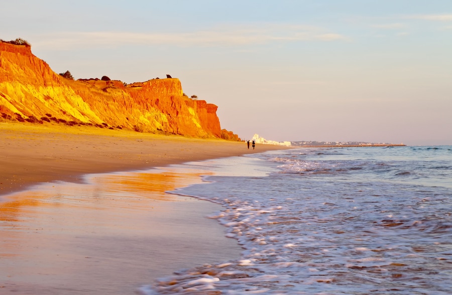 Beautiful Praia da Falesia near the city of Vilamoura with a shallow sandy beach fringed with unusual red rocks at sunset. Algarve, Portugal. Natural background. Summer holiday by the sea