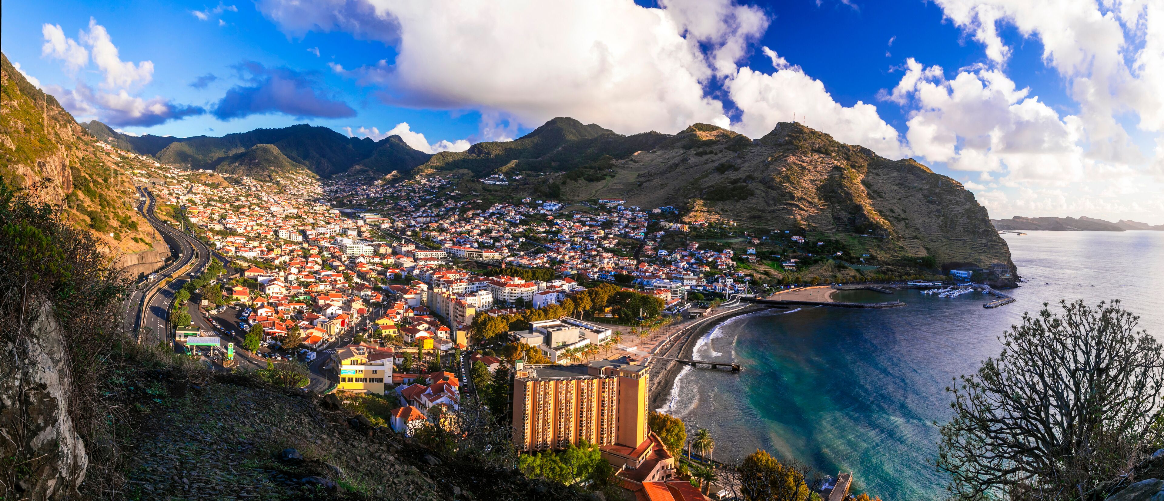 A coastal town with a winding road, a beach, and mountains in the background.