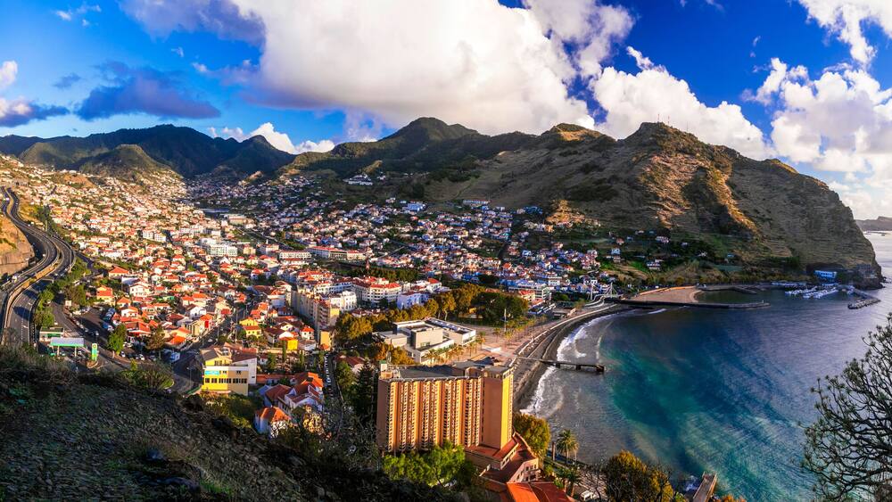A coastal town with a winding road, a beach, and mountains in the background.