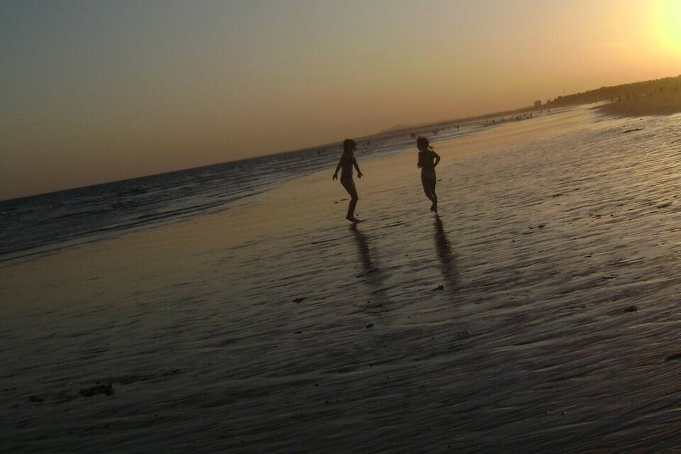 Uma praia ao pôr do sol com duas pessoas caminhando pela areia.