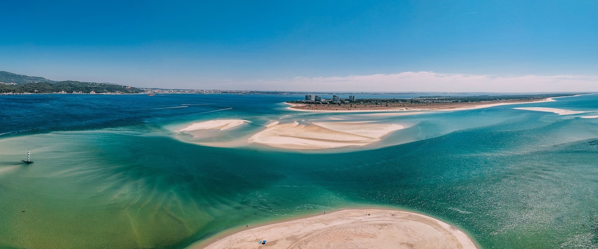 A coastal landscape with clear blue waters, sandy beaches, and distant hills.