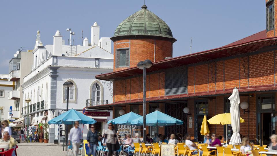 A bustling outdoor cafe with yellow and blue umbrellas, brick buildings, and a distinctive dome structure.