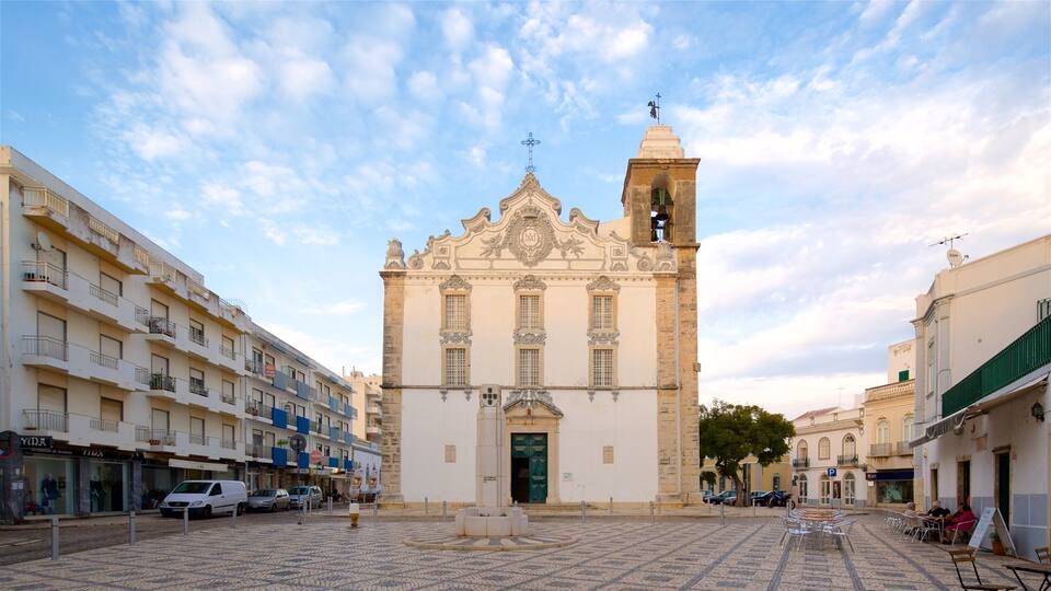 A historic church with a bell tower, surrounded by a cobblestone square with cafes and shops.