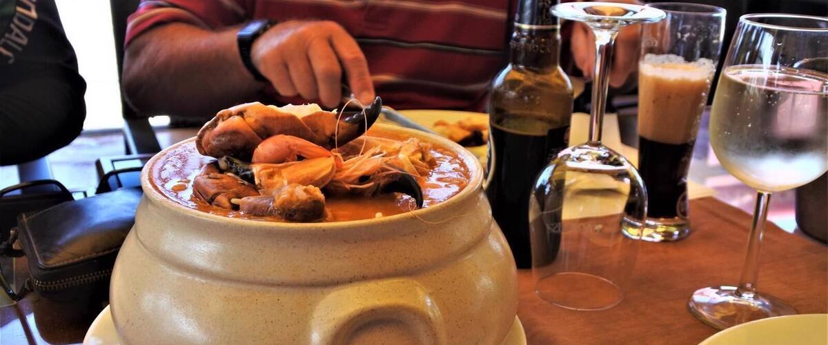 A large ceramic pot filled with seafood, placed on a table with glasses and bottles.
