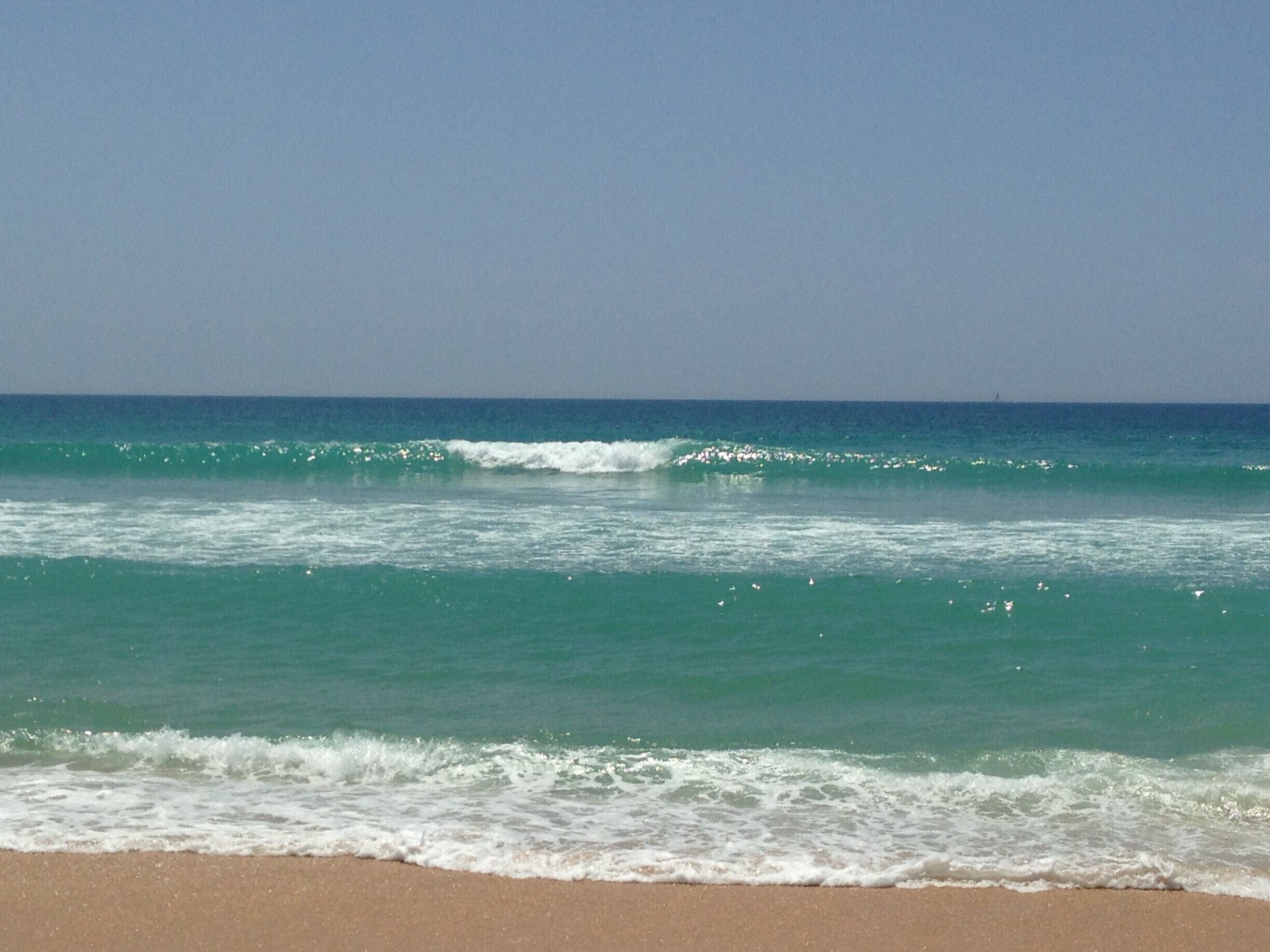 Una playa con olas turquesas y cielo despejado.