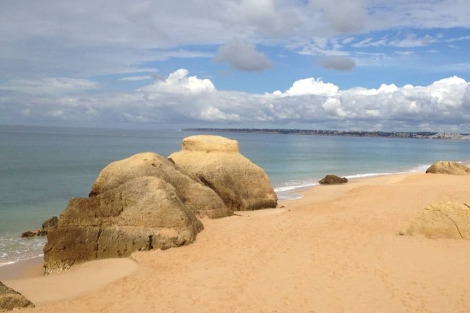 Une plage de sable avec de grandes formations rocheuses et un ciel dégagé parsemé de nuages.