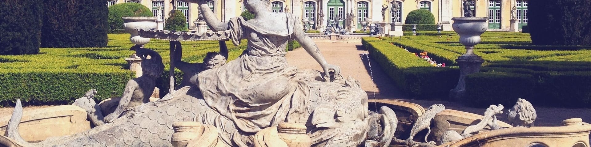 A classical fountain with a statue of a woman and a dragon in a garden.
