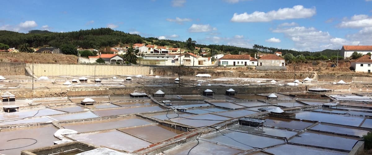 A salt evaporation pond with multiple rectangular basins, surrounded by residential buildings and a hilly landscape in the background.