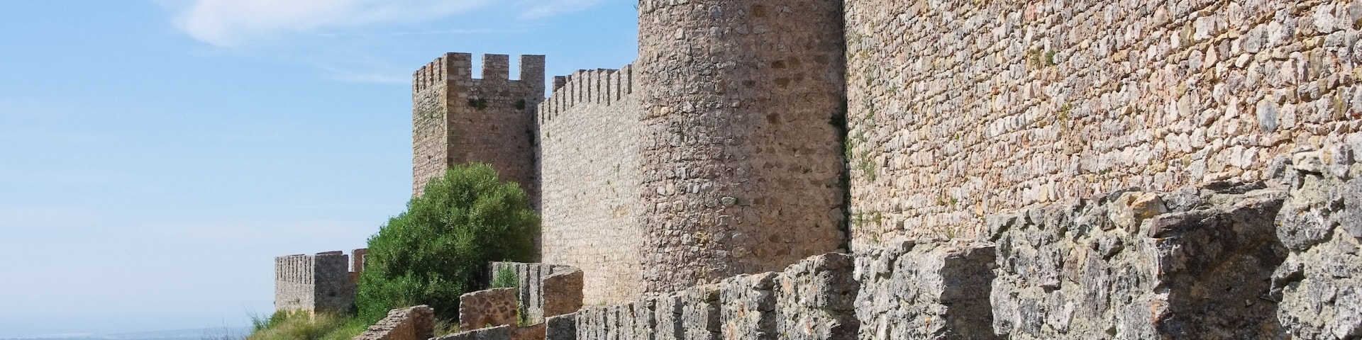 A medieval stone wall with crenellations and a tower.