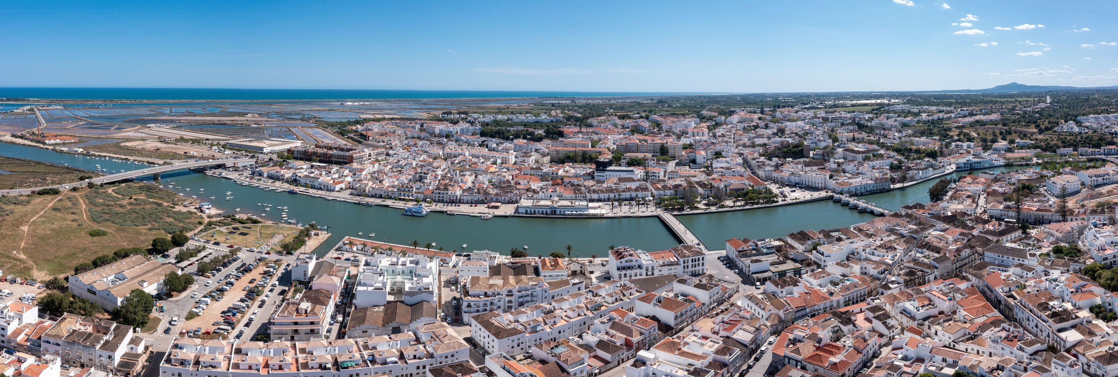 Tavira in Algarve is seen from above, featuring the river and white buildings with a clear sky. The view captures the town's layout and surrounding landscape. Panorama River Gilao and Roman bridge