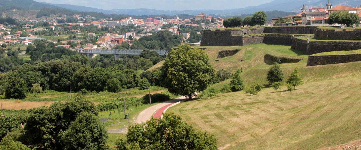 A historic town with a prominent castle on a hill, surrounded by lush greenery and rolling hills.