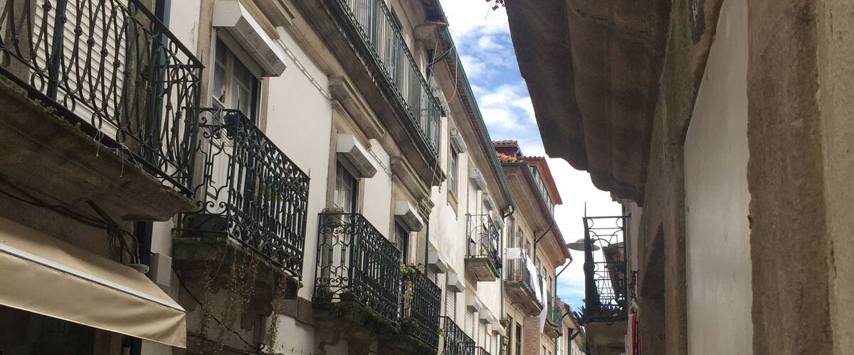 A narrow street with shops on either side, featuring balconies and a variety of merchandise.