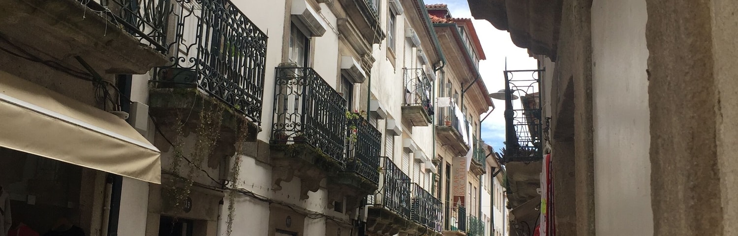 A narrow street with shops on either side, featuring balconies and a variety of merchandise.