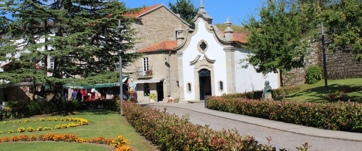 A church with a red-tiled roof, surrounded by a well-maintained garden with orange flowers and green shrubs.