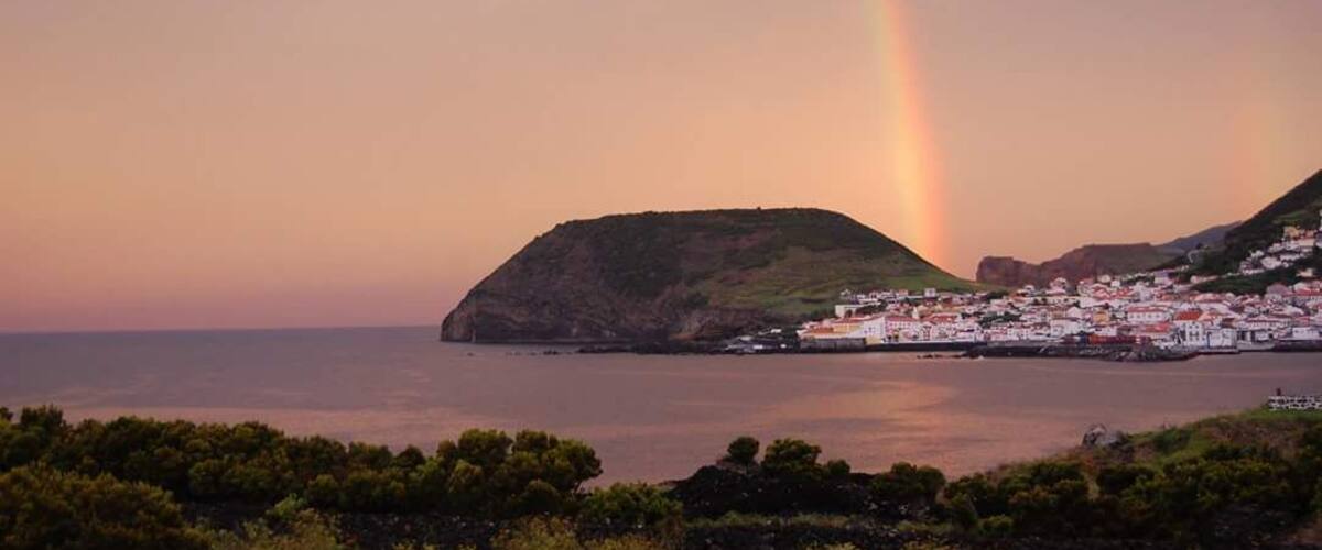 A coastal town with a prominent hill and a rainbow over the sea.