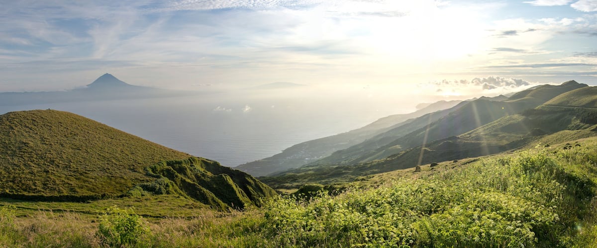 A mountainous landscape with a prominent hill in the foreground and a distant mountain peak.