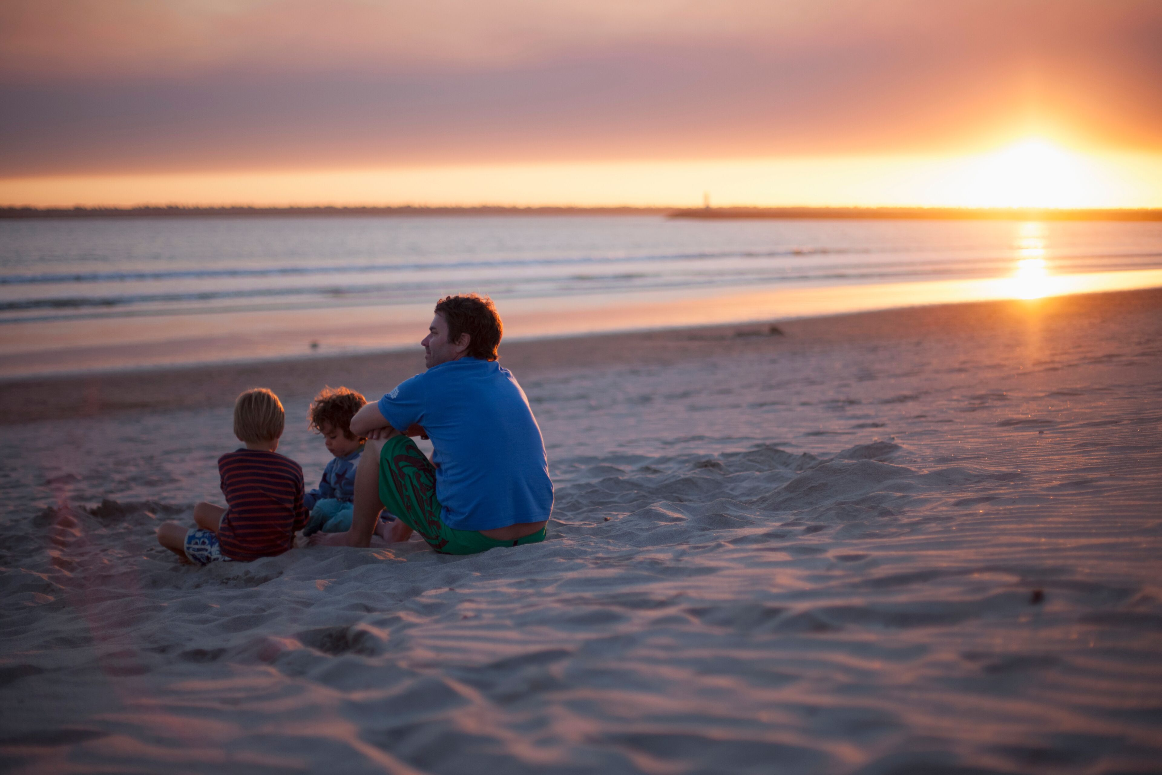Father with two kids sitting on beach during sunset, Viana do Castelo, Norte Region, Portugal