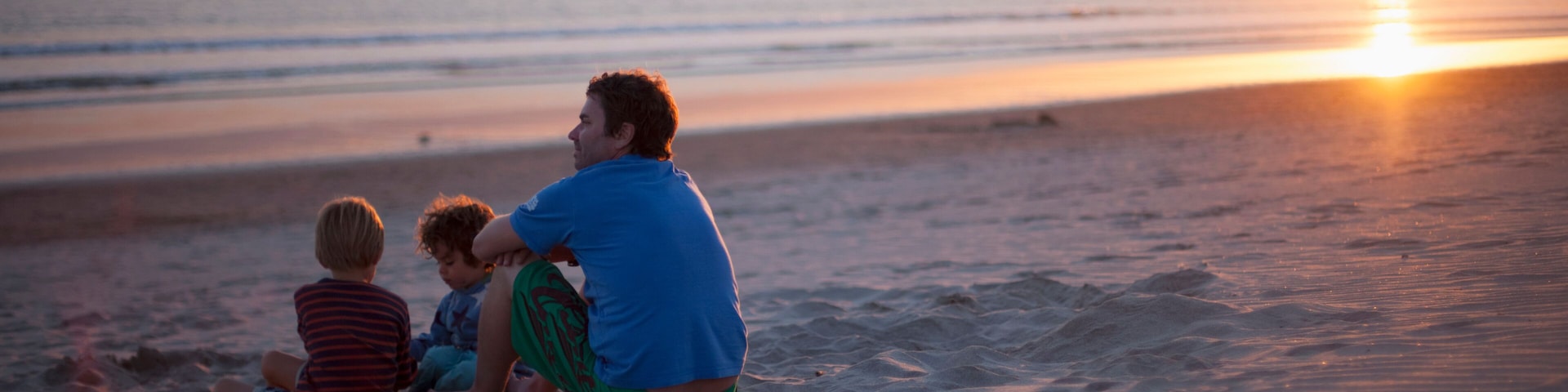 Um pôr do sol sobre uma praia com pessoas sentadas na areia.