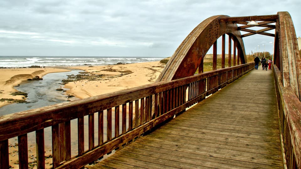 A wooden bridge over a beach with waves crashing nearby.