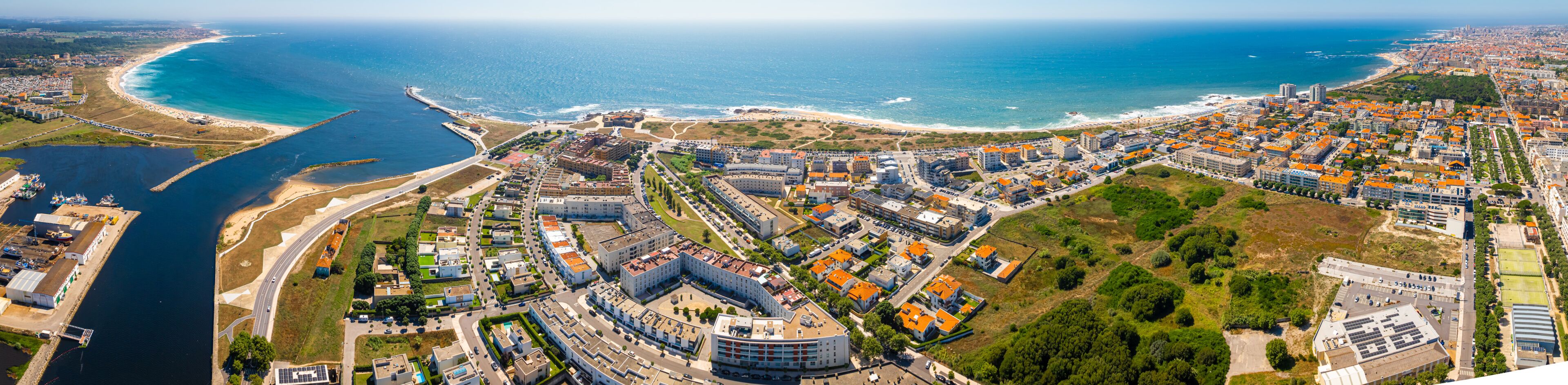 An aerial view of a coastal city with a marina, a beach, and dense urban development.
