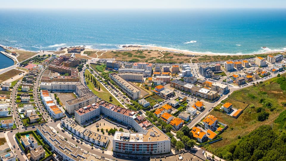 An aerial view of a coastal city with a marina, a beach, and dense urban development.