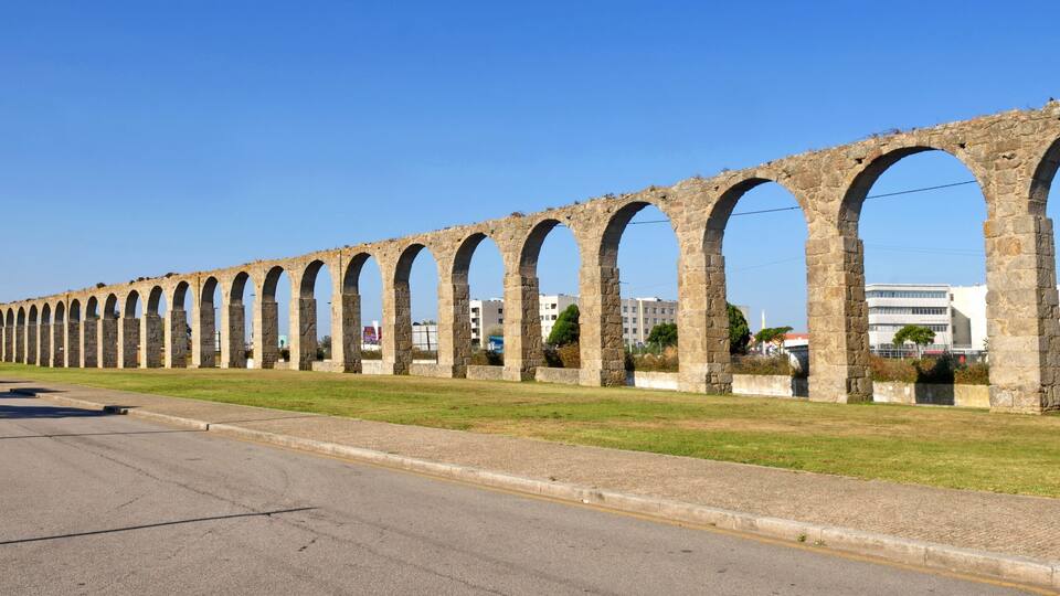 A series of stone arches along a road, with buildings in the background.