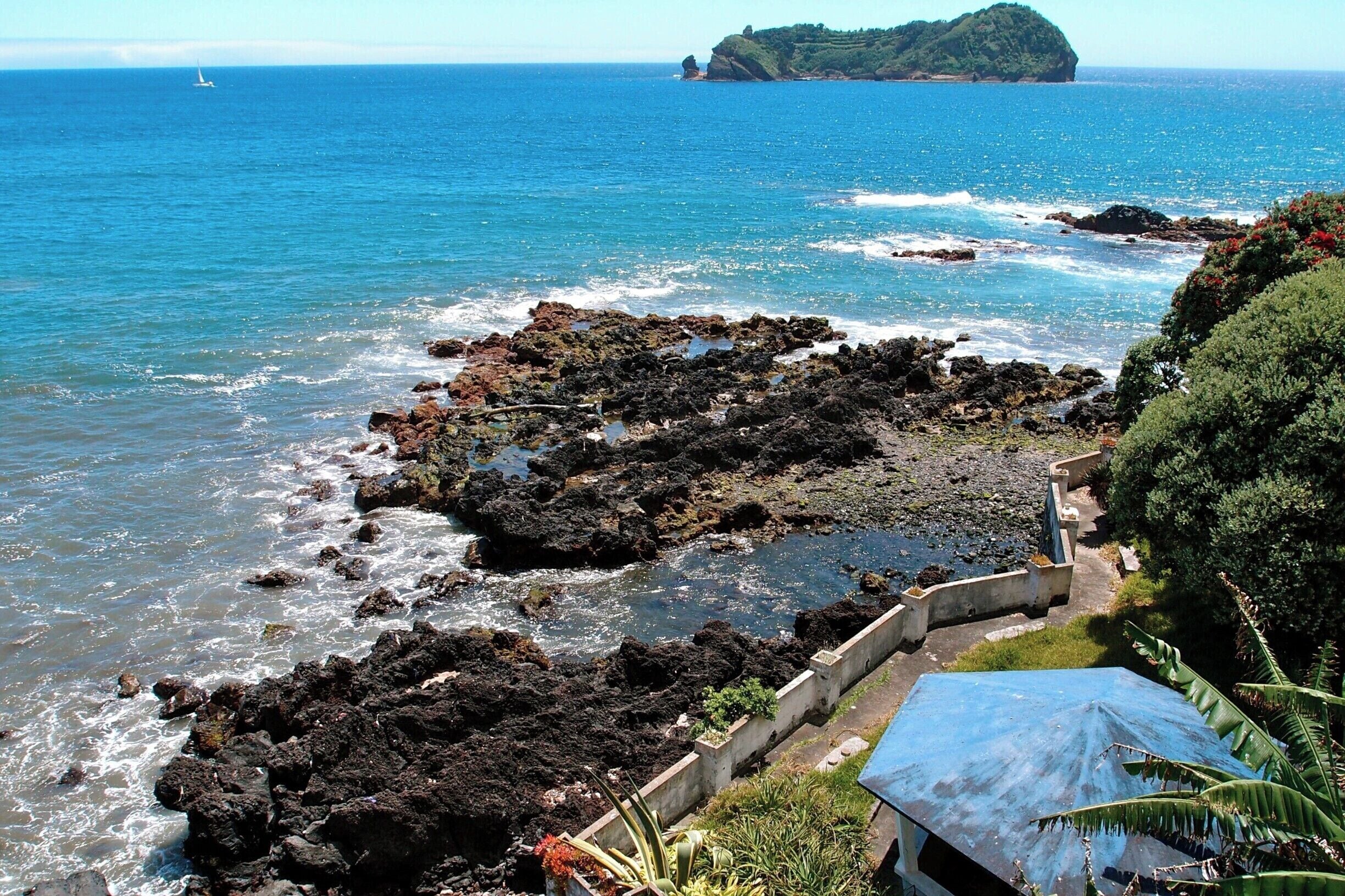 A #blue roof in an oceanside garden on the island of São Miguel in the Azores Archipelago; Ilhéu da Vila Franca sits on the horizon, a beautiful swimming hole in a volcanic crater.