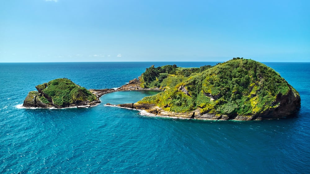 Un paysage côtier avec une grande île verdoyante entourée d’eaux turquoise.
