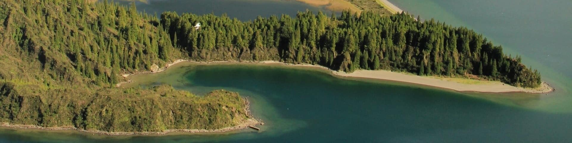 A coastal landscape with a bay, forested hills, and a clear sky.