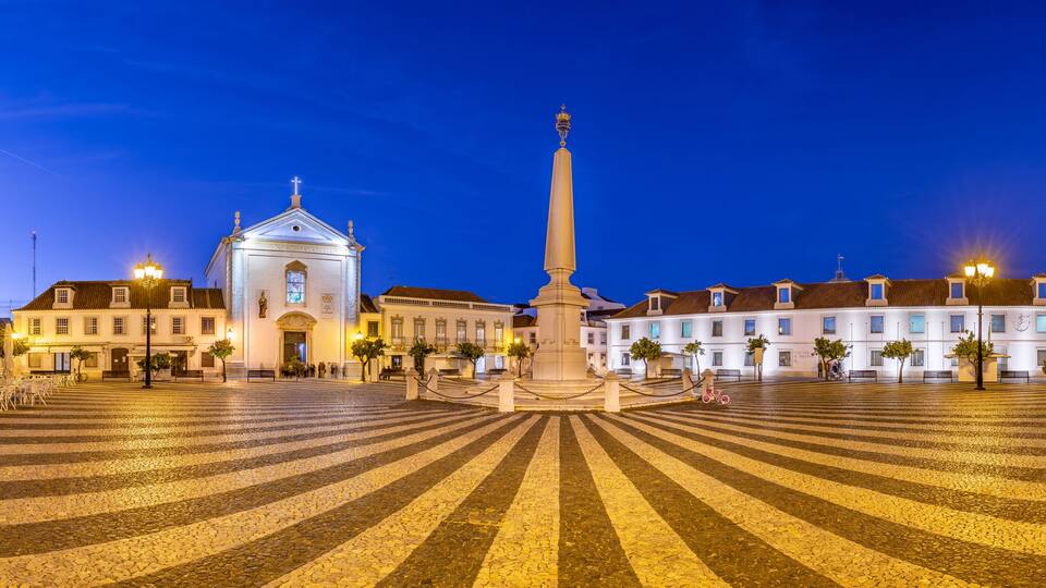 A historic square with cobblestone pavement, a central monument, and surrounding classical architecture.