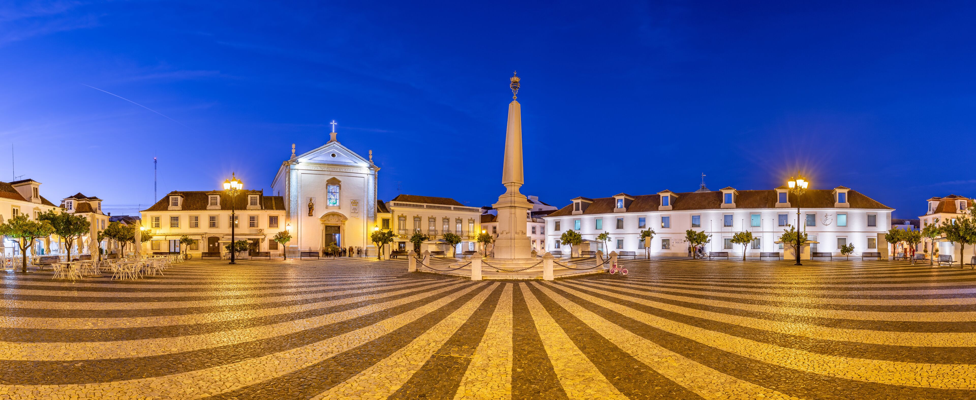 A historic square with cobblestone pavement, a central monument, and surrounding classical architecture.