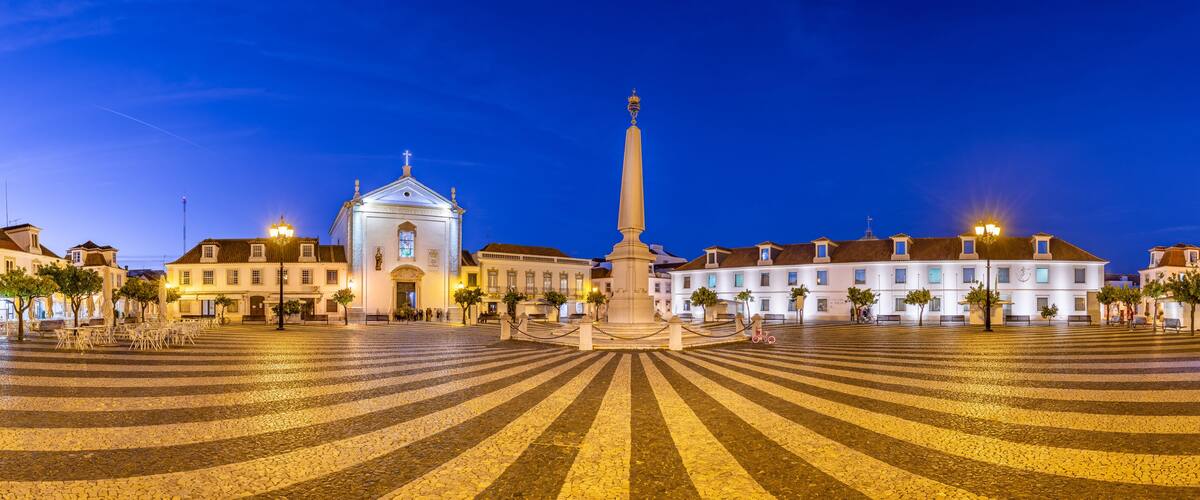 A historic square with cobblestone pavement, a central monument, and surrounding classical architecture.