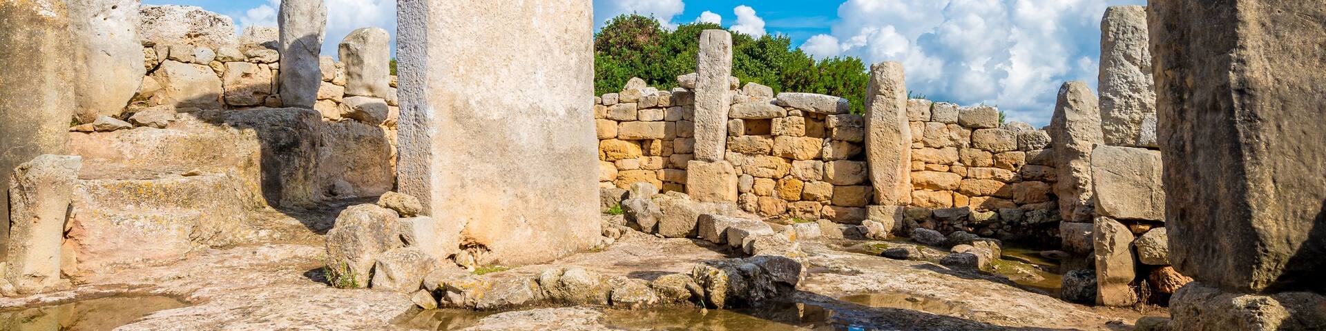 Ancient stone ruins with a large standing stone in the center, surrounded by smaller stones and a clear blue sky.