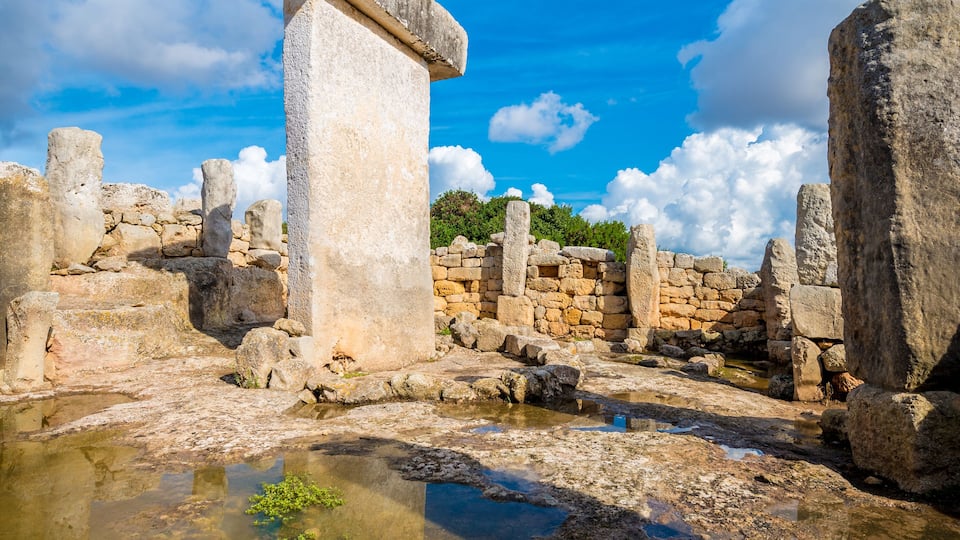 Ancient stone ruins with a large standing stone in the center, surrounded by smaller stones and a clear blue sky.