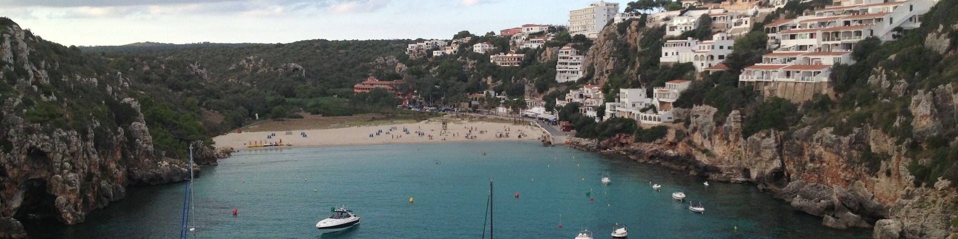 Un pueblo costero con barcos en el agua, una playa y edificios en una colina.