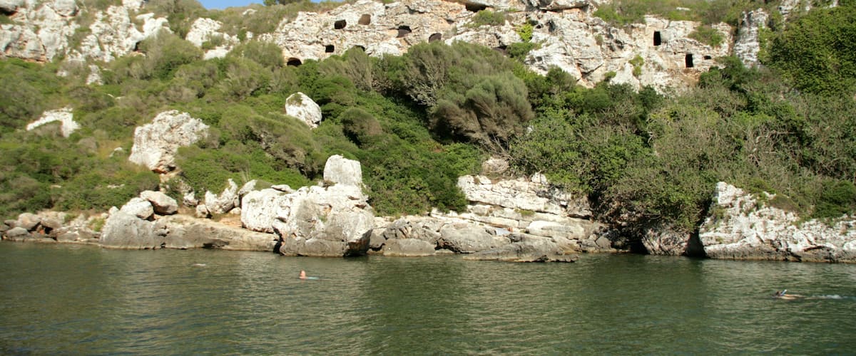 A rocky hillside with caves and a body of water.