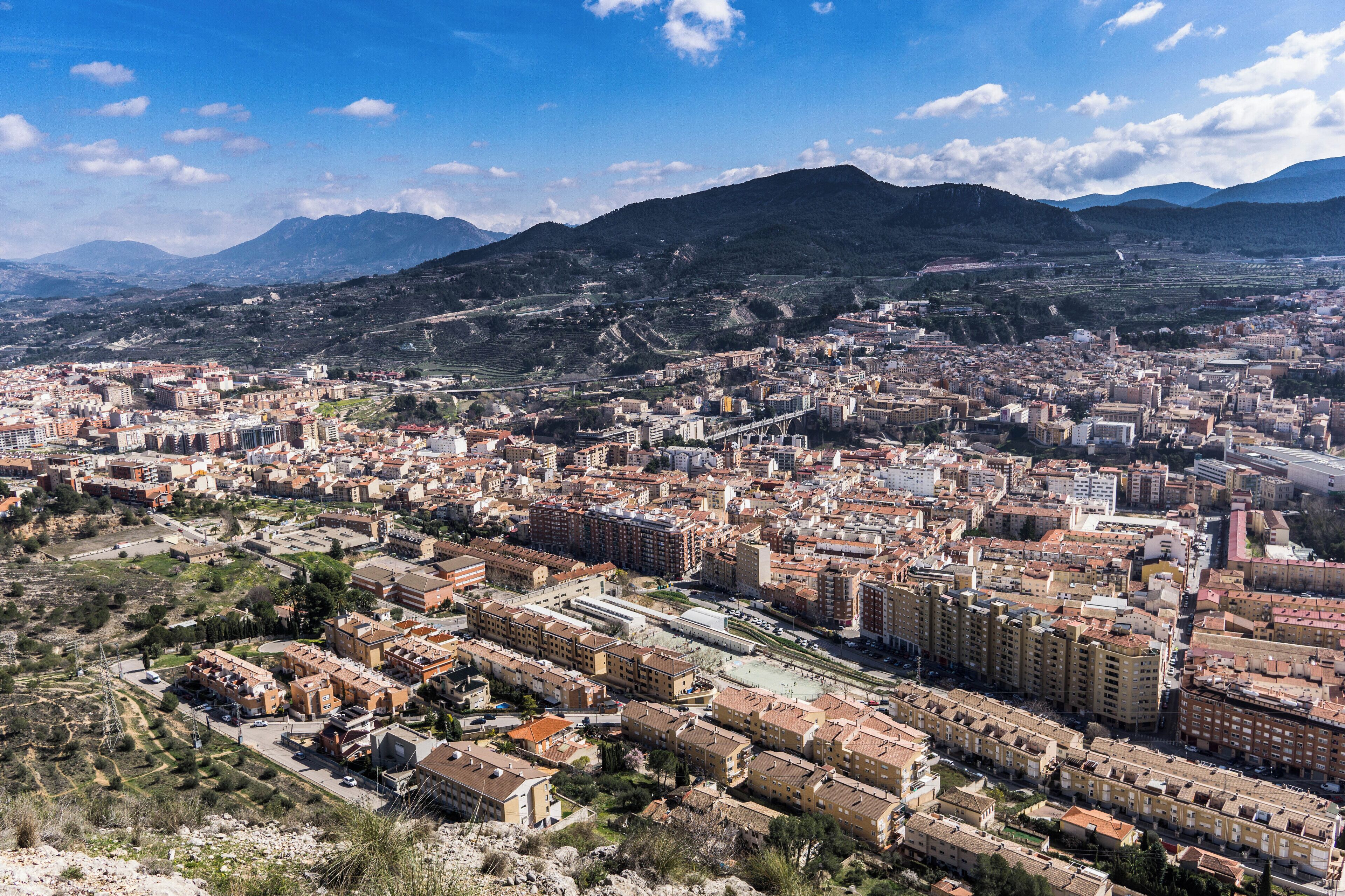 A cityscape with a mountainous backdrop, featuring dense urban buildings and a prominent bridge.
