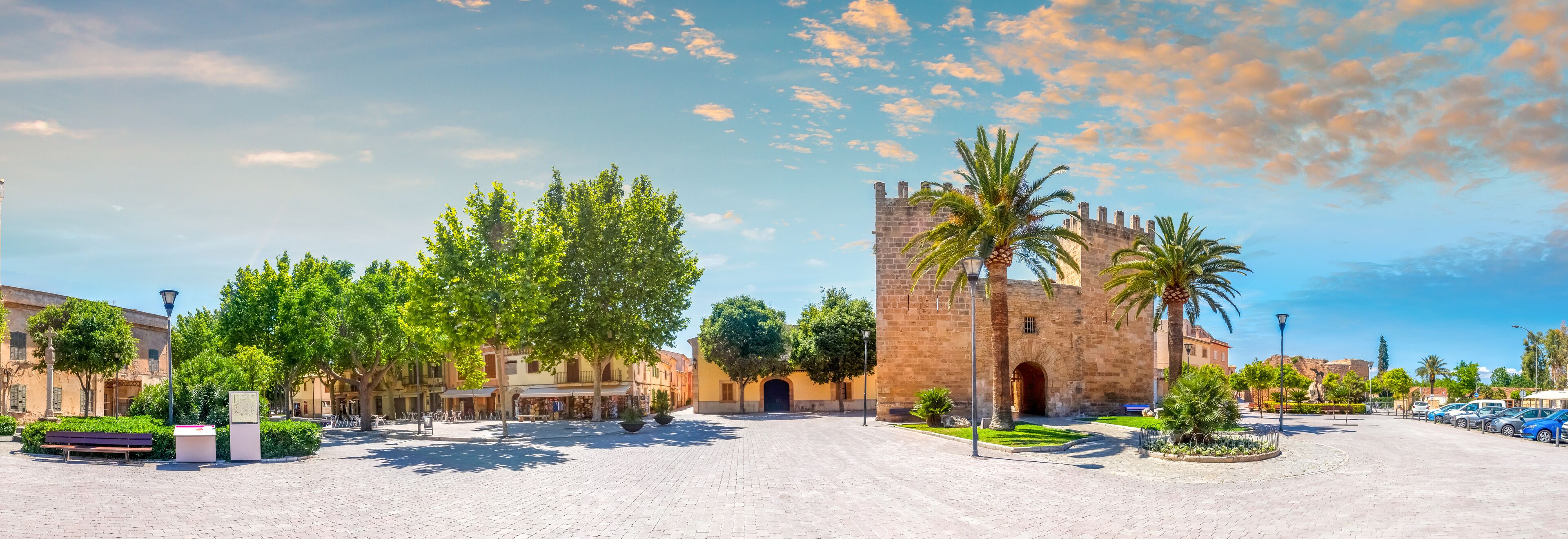 A historic square with a prominent tower, palm trees, and cobblestone streets.