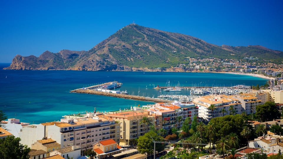 A coastal town with a marina, buildings, and a mountain in the background.