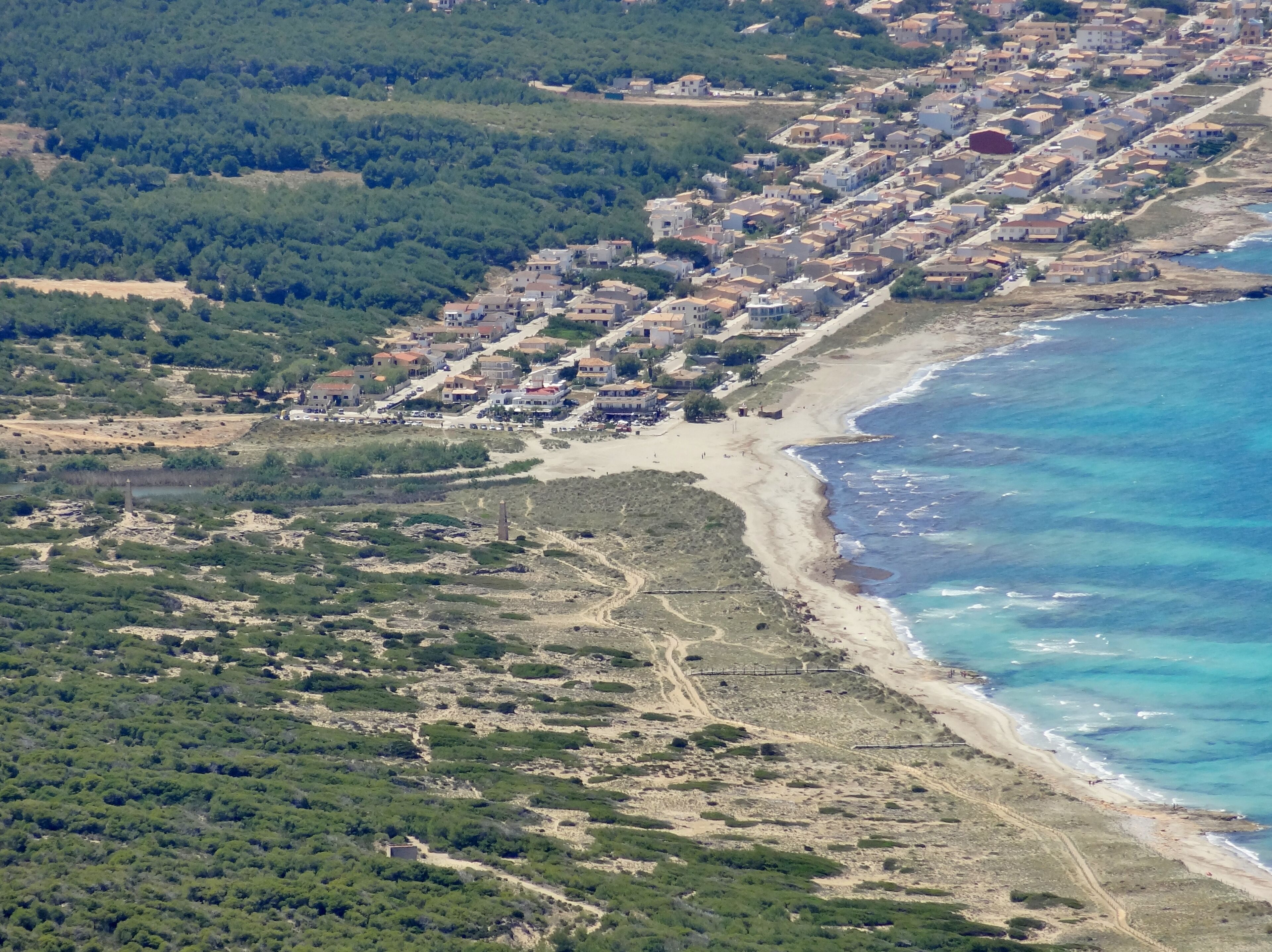 Vista aérea de un pueblo costero con playa, denso bosque verde y edificios residenciales.