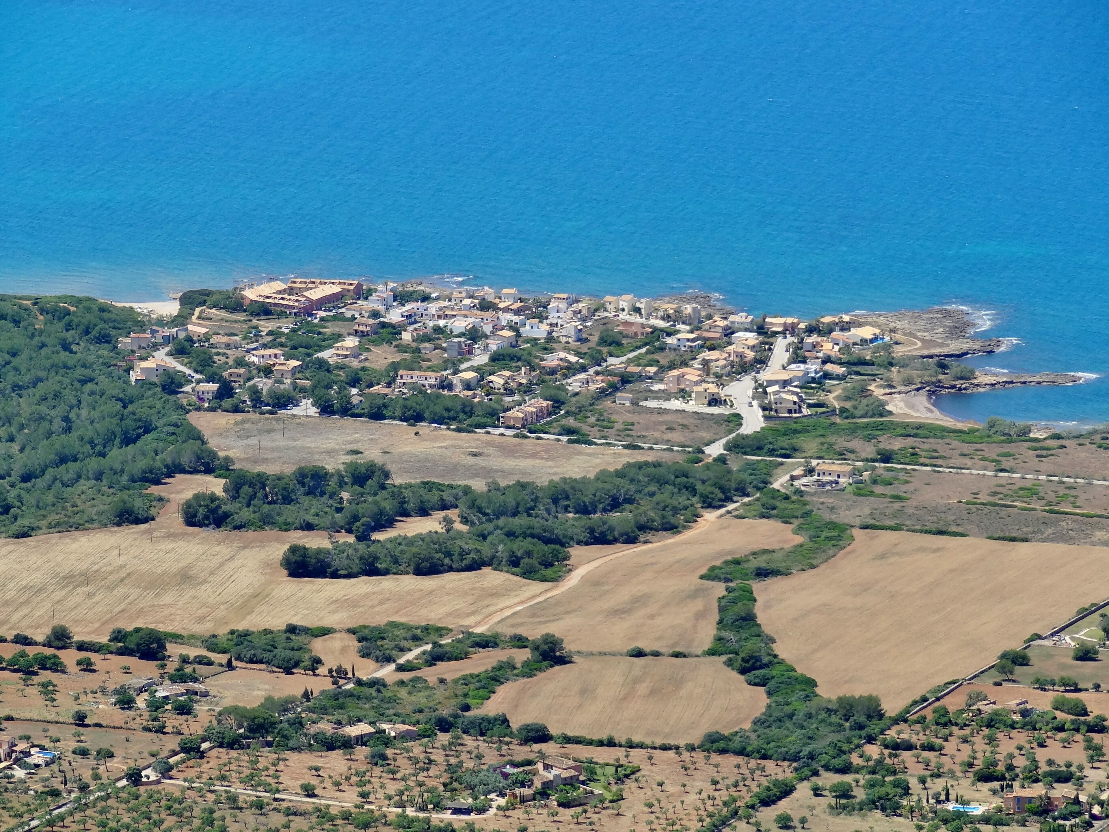 An aerial view of a coastal town with residential buildings, a beach, and agricultural fields.