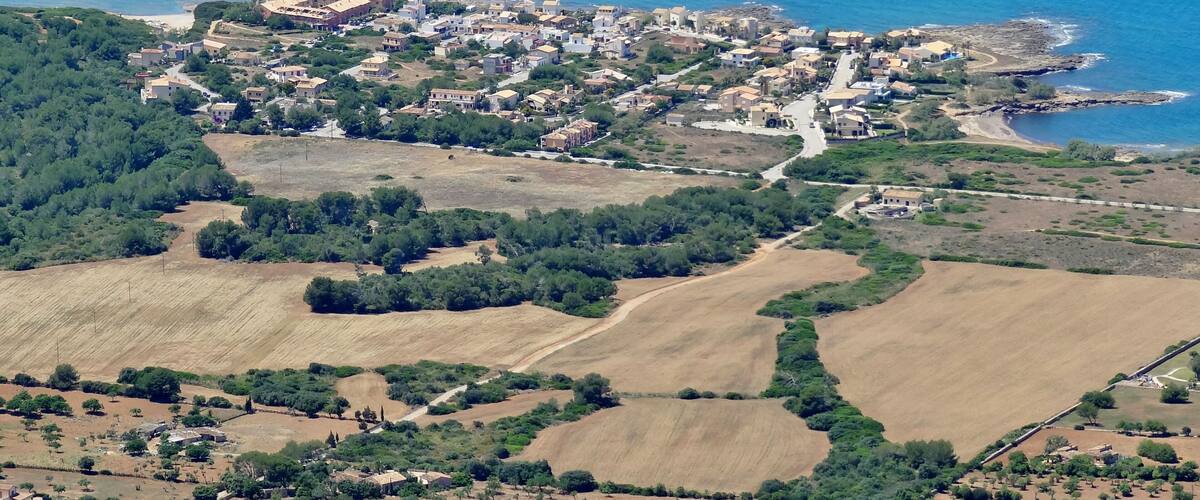 An aerial view of a coastal town with residential buildings, a beach, and agricultural fields.